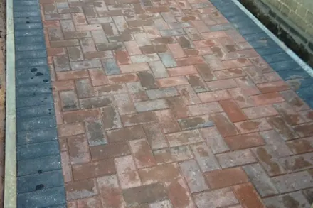 Narrow run of red brindle block paving with charcoal edges between two walls