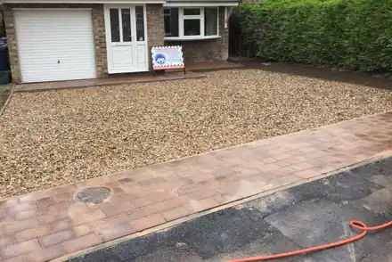 Gravel drive edged with warm-toned block paving in front of a garage